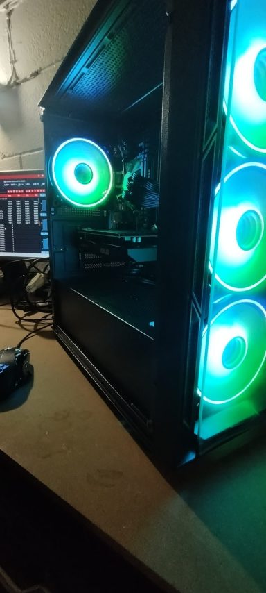 Intel Core i5-4460/16GB DDR3/256GB SSD/GTX1050 Ti 4GB A computer tower with glowing green and blue fan lights on a desk.